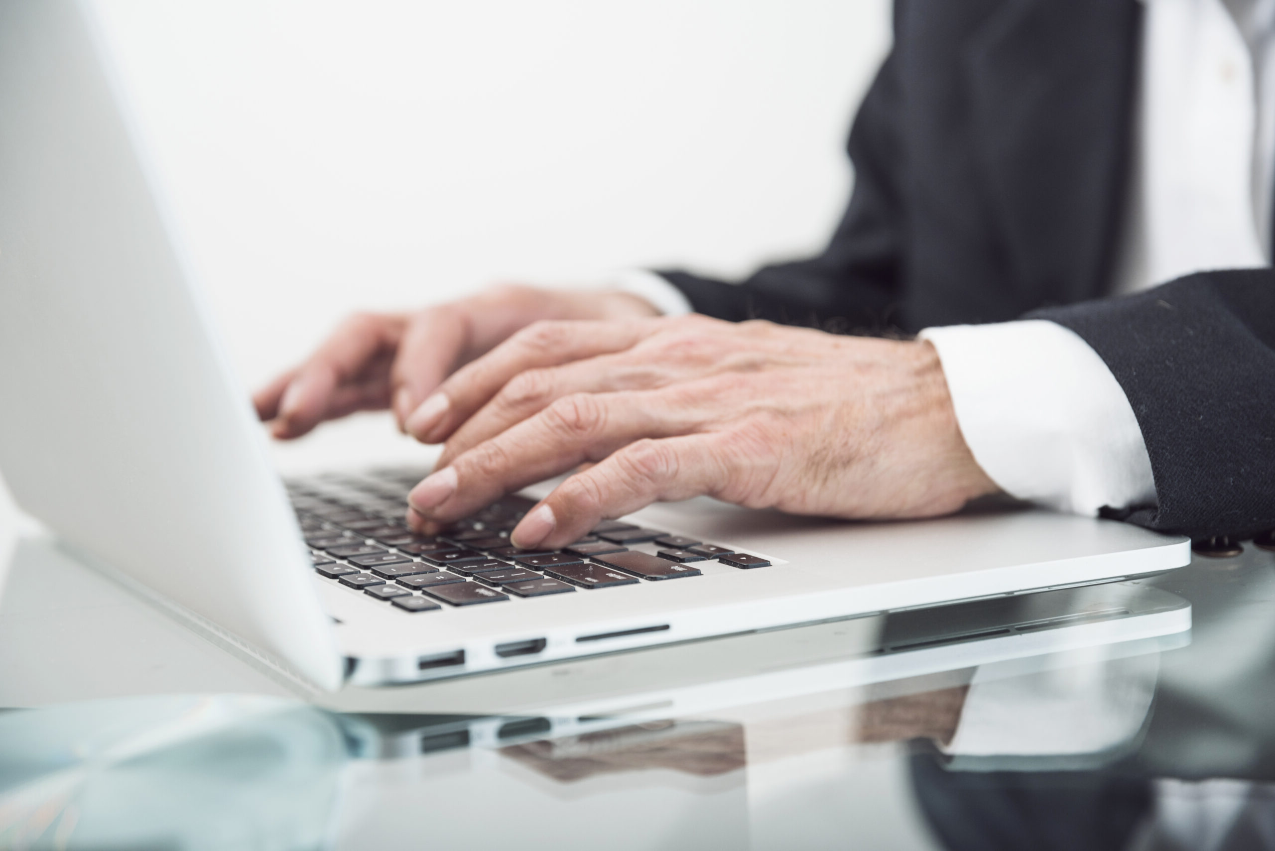close-up-senior-man-typing-laptop-glass-desk